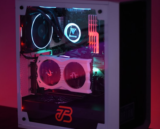 A gaming computer with visible internal components such as cooling fans and LED lights in a transparent case. The lighting emits a colorful glow with shades of purple, blue, and red.