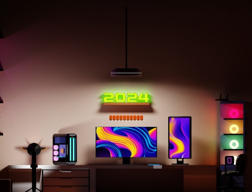 A modern gaming setup features a dual monitor arrangement with vibrant, abstract backgrounds. A glowing '2024' sign is mounted above the monitors. The desk includes a sleek gaming PC with LED accents, and the room is bathed in ambient lighting from multiple RGB light sources. Shelves with decorative items and a chair complete the workspace.